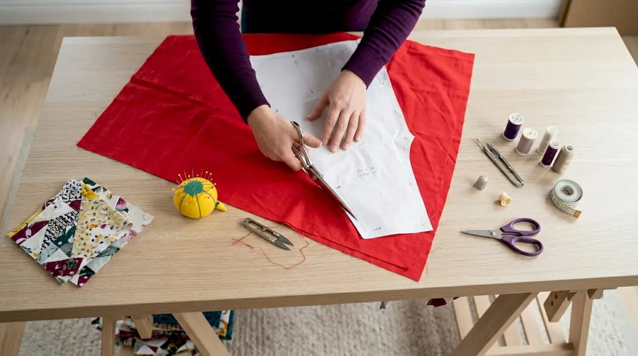 Hands cutting fabric with paper pattern